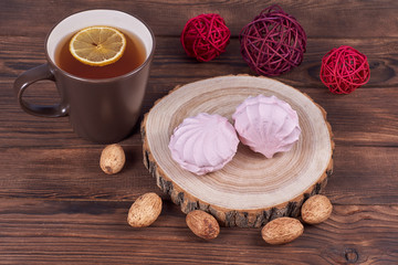 Two zephyrs with raspberries on a wooden stand next to brown cup with lemon tea, nuts and various decorative elements on the dark wooden background