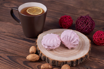 Two zephyrs with raspberries on a wooden stand next to brown cup with lemon tea, nuts and various decorative elements on the dark wooden background