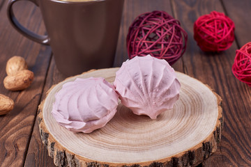 Two zephyrs with raspberries on a wooden stand next to brown cup, nuts and various decorative elements on the dark wooden background