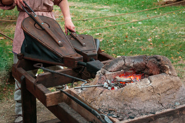 Blacksmith in ancient clothes squeezing bellows to kindle fire in medieval furnace. Reconstruction