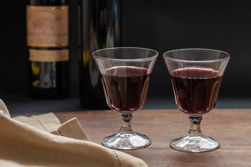 Two glasses of red wine on wooden table, dark background