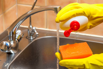 gloved hands with dishwashing liquid and a sponge in the kitchen closeup