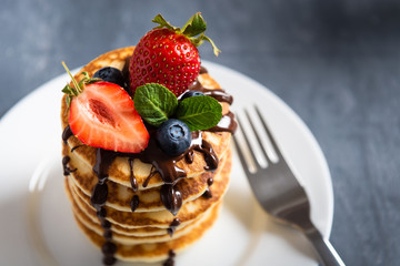 Tasty pancakes with strawberry and chocolate sauce on dark background. Copy space. Close up, side view