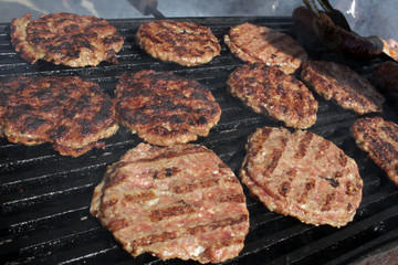 Burgers on a grill. Grilled meatballs on a BBQ. Roasted minced meat on a barbecue. Grilled burgers. Fast food on the street. Healthy or unhealthy food concept.