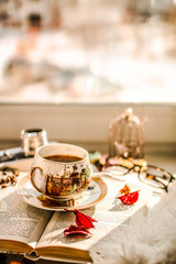 Cup of tea, open book and flowers near the window. Morning composition.