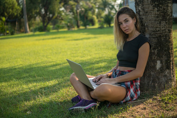 pretty adult girl resting under the tree outside, holding a laptop on her knees,