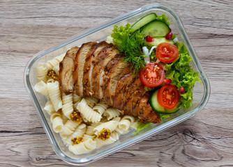 Lunch box: rotini with baked chicken breast and salad on a wooden background. Top view, flat lay. Delicious healthy lunch. The concept of healthy eating.
