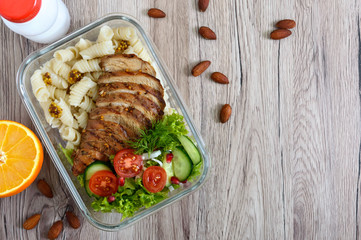 Lunch box: rotini with baked chicken breast and salad on a wooden background. Top view, flat lay. Delicious healthy lunch. The concept of healthy eating.