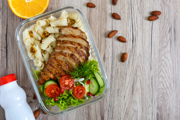 Lunch box: rotini with baked chicken breast and salad on a wooden background. Top view, flat lay. Delicious healthy lunch. The concept of healthy eating.