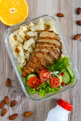 Lunch box: rotini with baked chicken breast and salad on a wooden background. Top view, flat lay. Delicious healthy lunch. The concept of healthy eating.