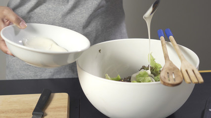 Woman pouring salad cream to white bowl for mix salad vegetable.