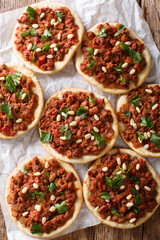 Fototapeta na wymiar Beef Sfiha Lebanese mini pizzas topped with ground beef, onions, tomato, and pine nuts closeup. Vertical top view