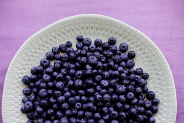 Blueberries in a plate on a table with a colored cloth.