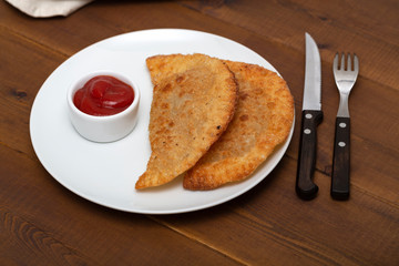 Chebureks - fried pie with meat and onions. White plate with fried chebureks on a wooden table.