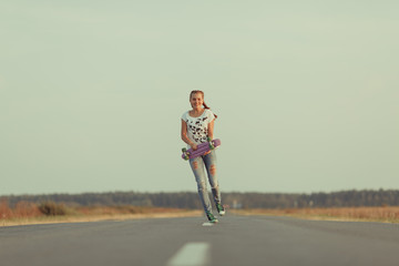 Fototapeta premium Young happy cute girl rides skateboard on road, outdoor