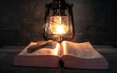 wooden cross on bible with light of oil lamp in worship room. christian concept.