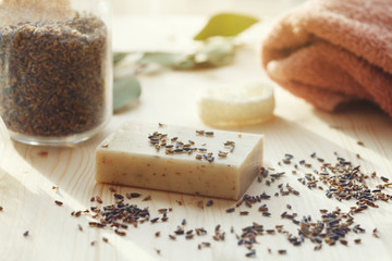 handmade lavender and coconut soap, lavender flowers in glass bottle, luffa sponge and soft towel on wooden table, natural body, face and hair care, sunny morning