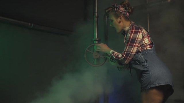A lot of steam starts coming while a woman in pin up style is turning a valve, slow motion