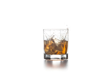 Whiskey splash from the fallen ice cube into glass with beverage on light background..