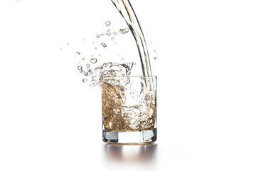 Whiskey pouring into glass with ice on light background..