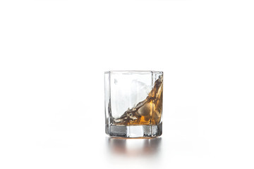 Whiskey splash in glass with ice on light background..