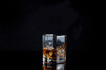Whiskey splash from the fallen ice cube into glass with beverage isolated on black background..