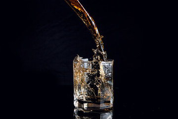 Whiskey pouring into glass with ice isolated on black background..
