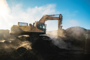 Yellow big excavator in the coal mine, loads the breed, with the bright sun and nice blue sky in...