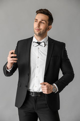 Handsome man with bottle of perfume on grey background