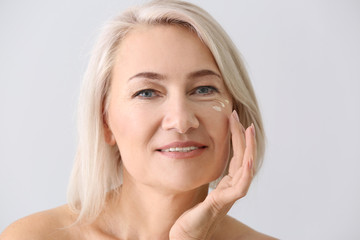 Mature woman applying face serum on light background