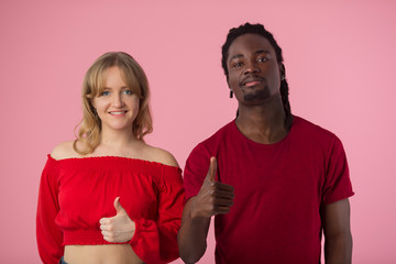 beautiful young couple african man and white woman in red t-shirts on pink background with hand gesture