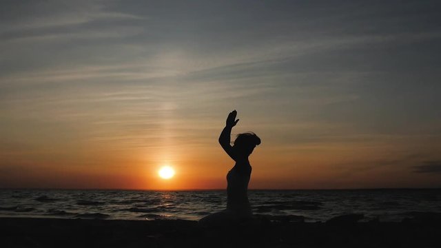 woman doing yoga on the beach on the background of the water and the sunset, silhouette. kundalini yoga