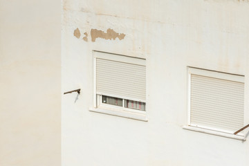Two windows closed with roller shutters on a hot summer day in Spain. Isolated on white wall.