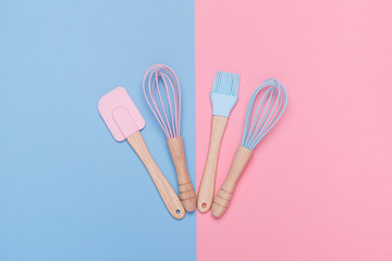 top view of the set of pastel colored whisk, spatula and pastry brush on pastel pink and blue background
