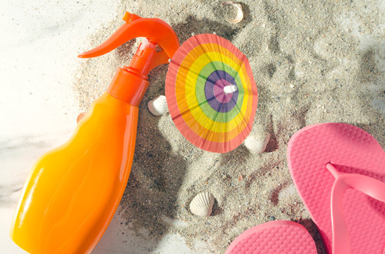 Top view of sunscreen,flip flop,little beach umbrella on sandy shore.Warm colors
