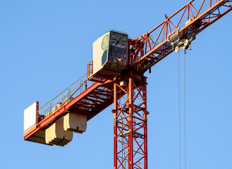 Naklejka premium Construction crane tower on blue sky background. Crane and building working progress. Red lifting faucet. Empty Space for text. Construction concept. Site. New buildings with a crane. Tower crane