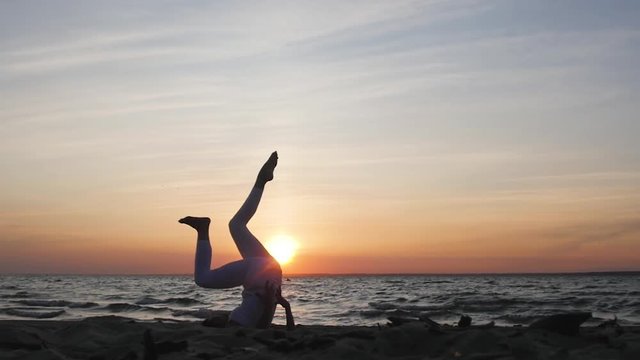 woman doing yoga on the beach on the background of the water and the sunset, silhouette. kundalini yoga