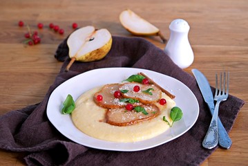 Polenta with cheese, caramelized pear and red currants on a white plate. Italian food. Selective focus.