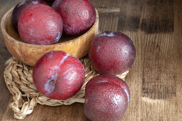 Top view of plums in wooden bowl on esparto base and wooden background