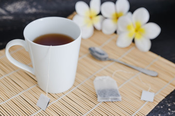 cup of dark tea on bamboo placemat with spoon and flowers all around