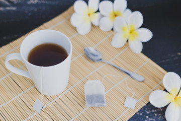 cup of dark tea on bamboo placemat with spoon and flowers all around