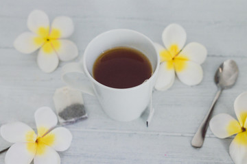 cup of dark tea on wooden table with spoon and flowers all around