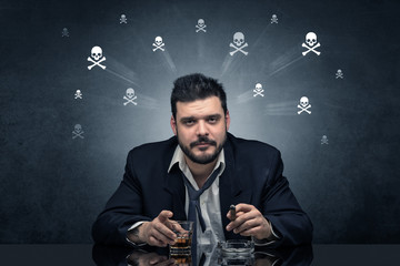 Loser drunk man sitting at table with skulls concept around
