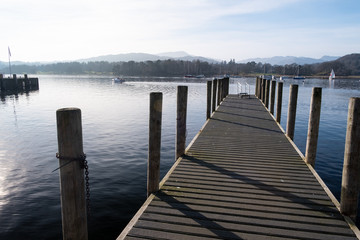 Fototapeta premium The pier at Ambleside Waterhead on a clear day looking over the Great Langdale skyline, Lake District, UK