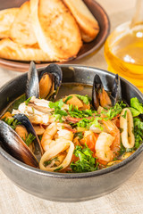 Homemade cioppino in a bowl and toast on a light rustic background - Italian-American seafood soup - fish, mussels, shrimp and squid.