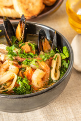 Homemade cioppino in a bowl and toast on a light rustic background - Italian-American seafood soup - fish, mussels, shrimp and squid.