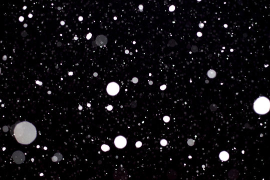 Large flakes of snow against the black sky, swirling in the light of lantern. - Image