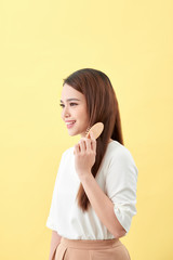 Portrait of cute young woman on yellow background combing hair.