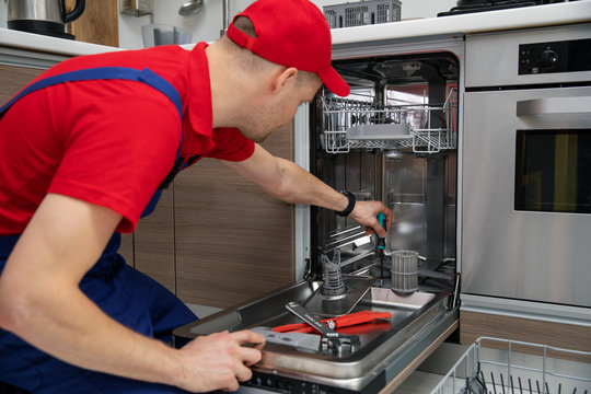 home appliance maintenance - repairman repairing dishwasher in kitchen