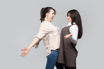 Portrait of two funny beautiful brunette best friends in casual style, raised arms standing face to face and having fun together. indoor studio shot, isolated on grey background.